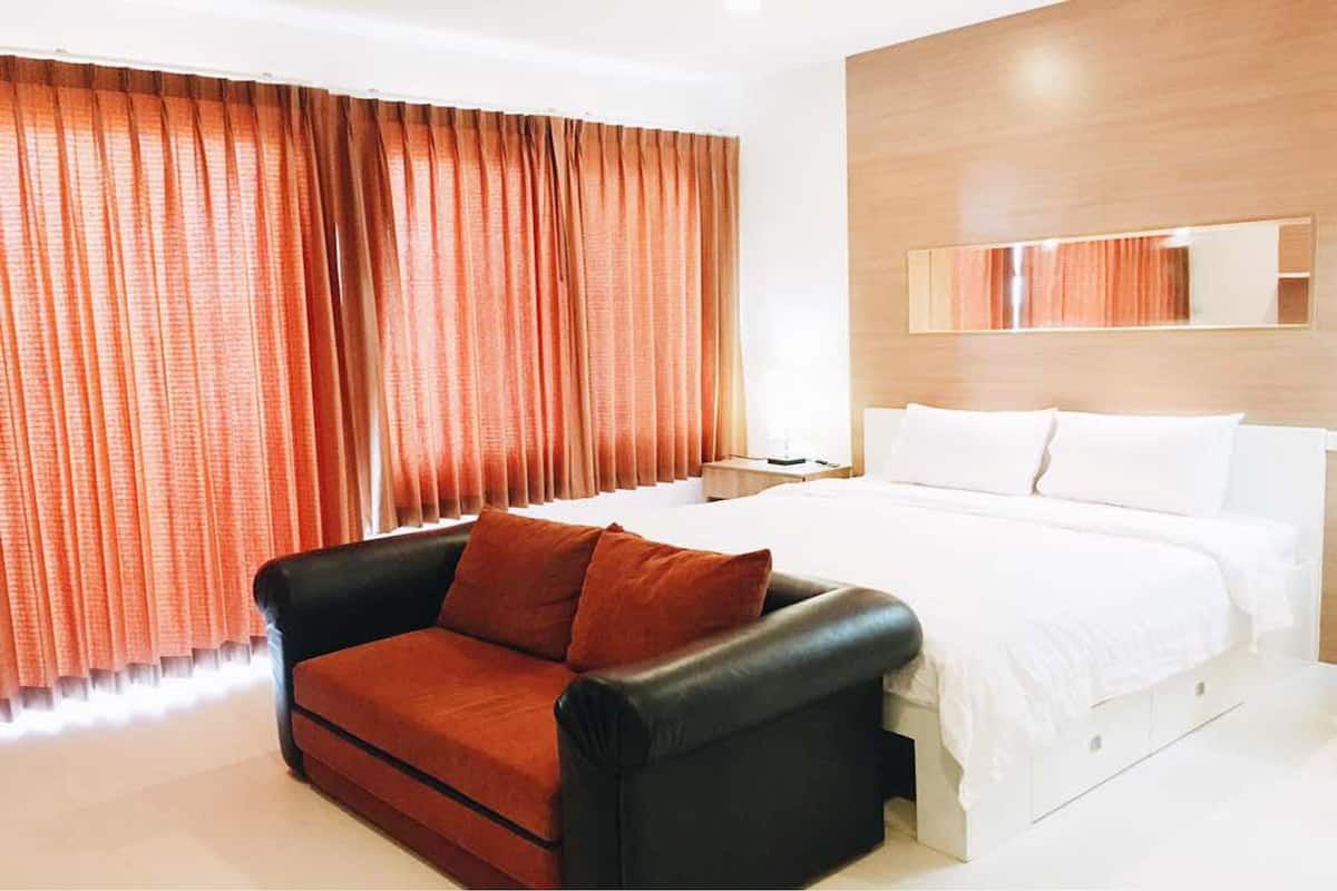 A modern hotel room with a large bed, a black leather sofa, and orange curtains.