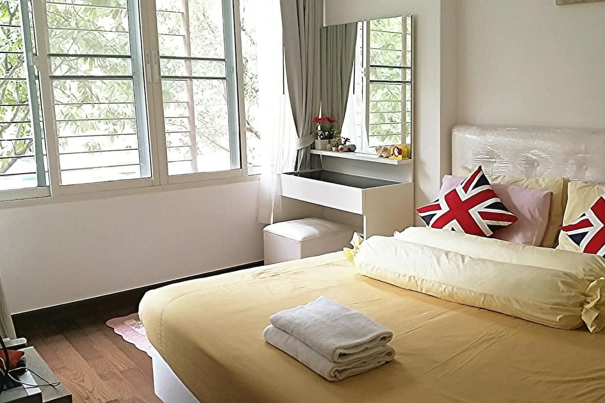A neatly made bed with a white duvet, pillows with Union Jack designs, and a folded towel on the bed.