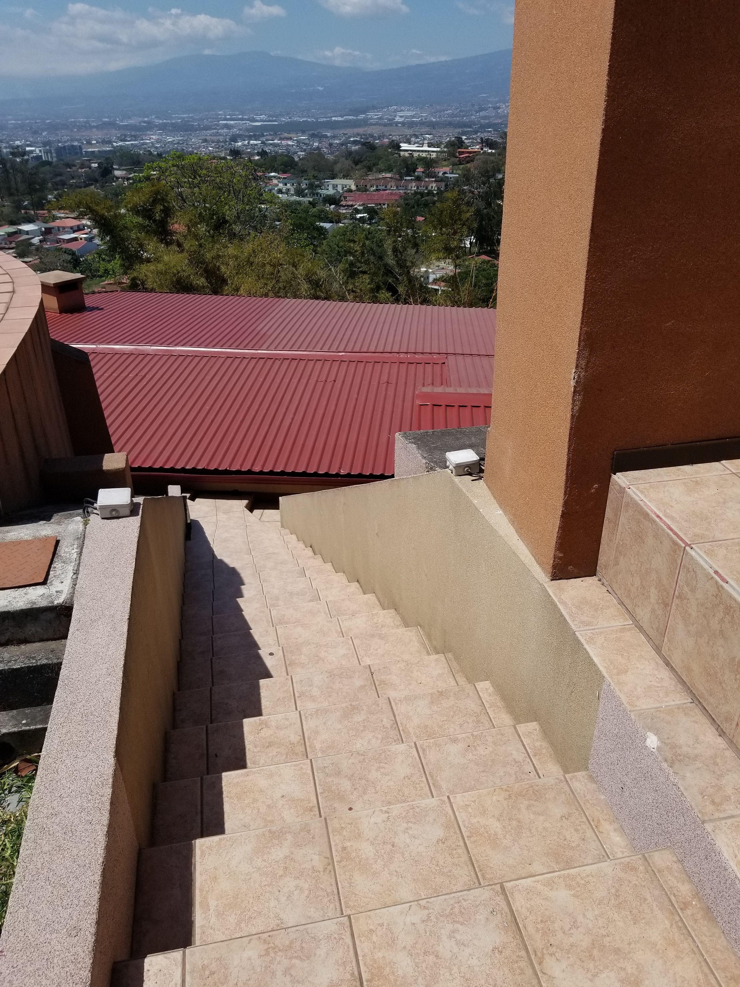 A staircase leading to a red-roofed building with a view of a cityscape and mountains in the distance.