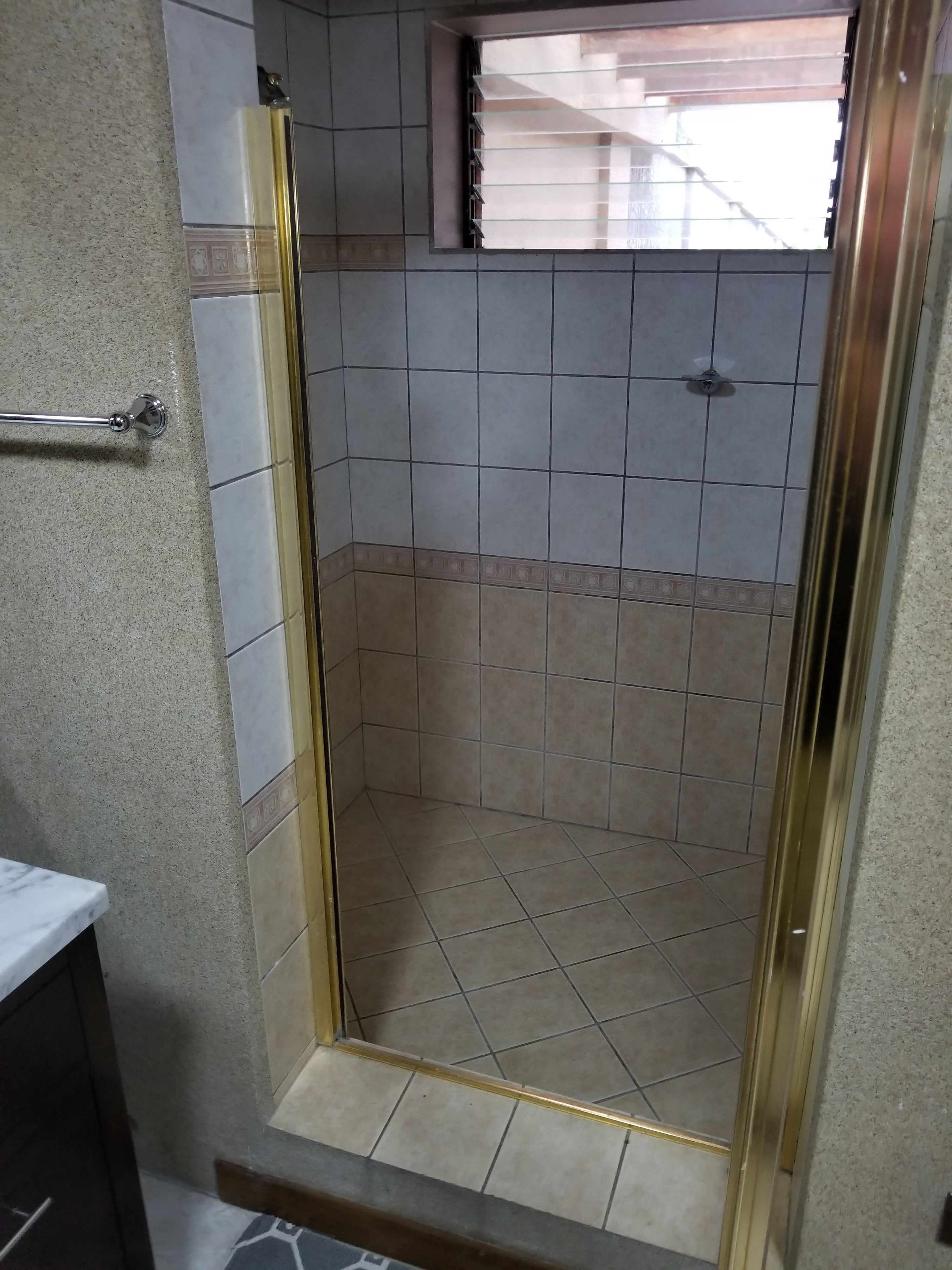 A small, enclosed shower area with tiled walls and floor, a glass door, and a window above.