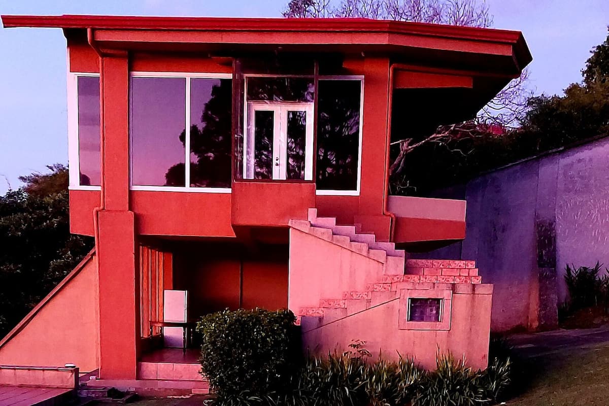 Ein modernes Haus mit roter Fassade, einem Vorgarten und einem kleinen Pool.