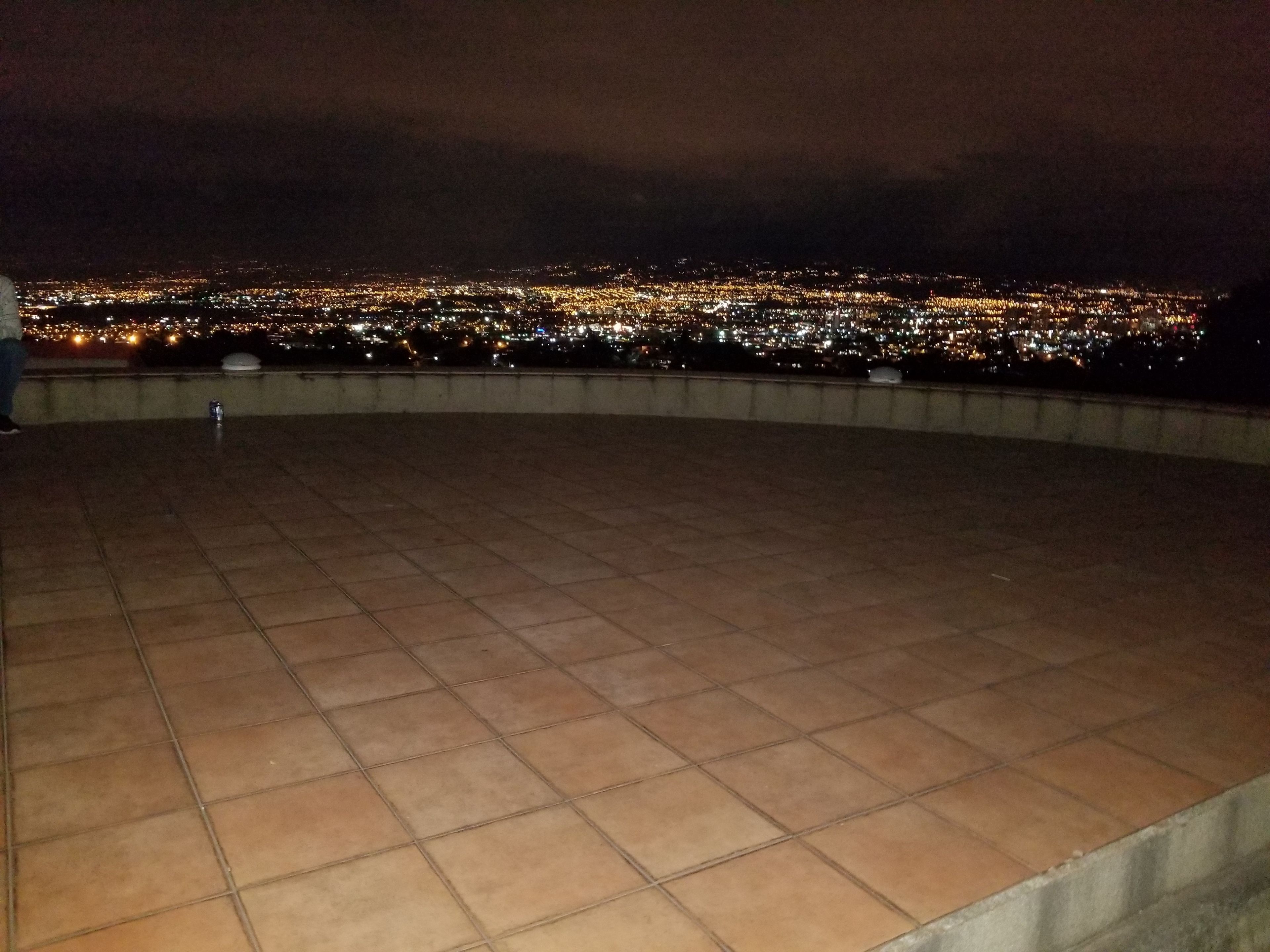 A tiled terrace with a panoramic view of a city at night.