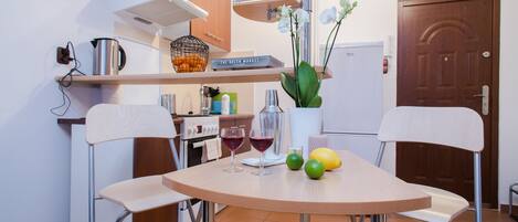 A compact kitchen with a round table, two chairs, a refrigerator, a stove, and a door.