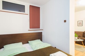 A bedroom with a wooden headboard, a bed with green patterned bedding, a window with a blind, and a small table with a plant. - ShortStayPoland Graniczna (Warsaw)