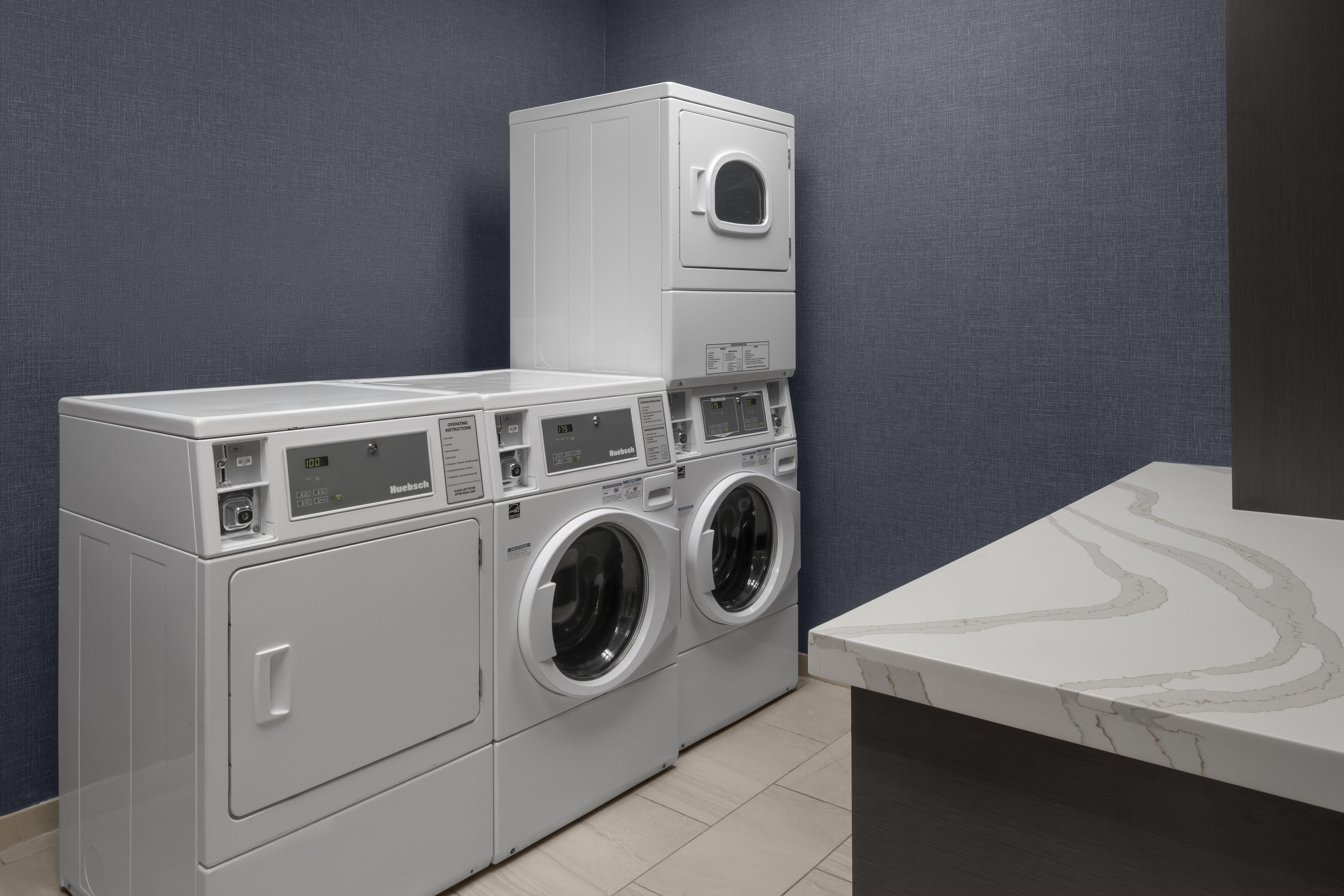 Une buanderie équipée d’un lave-linge et d’un sèche-linge superposés, d’un plan de travail en marbre et d’un mur à texture.