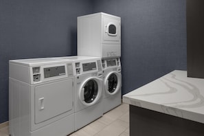 A laundry room with a stacked washer and dryer, a marble countertop, and a textured wall. - Hilton Garden Inn Roslyn (Port Washington)