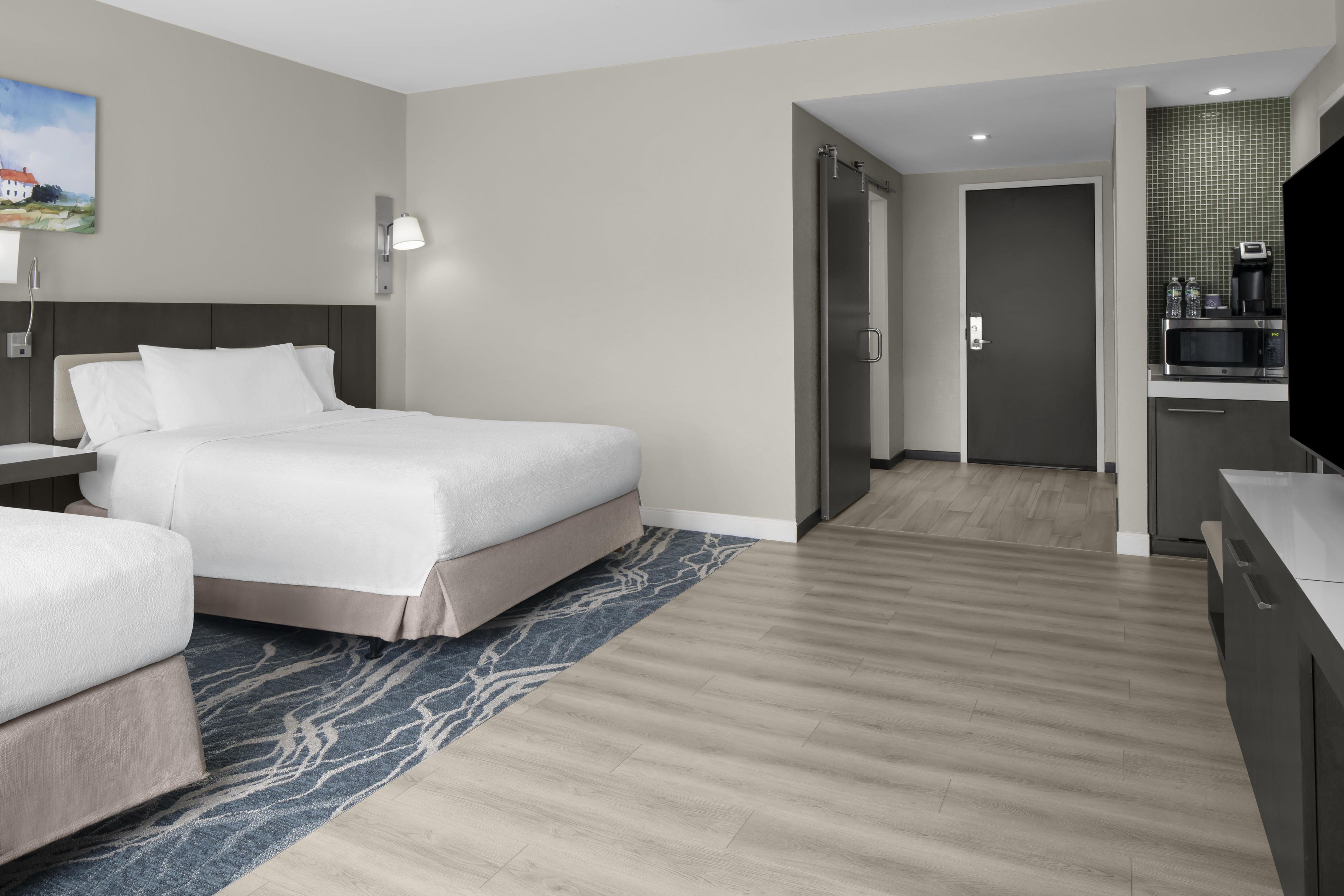 A hotel room with a bed, bedside tables, a flat-screen TV, a microwave, and a small kitchenette.