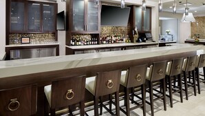 A modern kitchen with a long island counter, bar area, and built-in cabinets. - Hilton Garden Inn Roslyn (Port Washington)