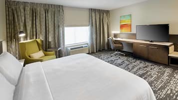 Quarto de hotel com uma cama grande, uma mesa com cadeira, televisão e janela com cortinas.