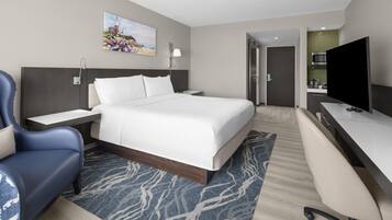 A hotel room with a bed, a desk, a chair, a television, and a painting on the wall.