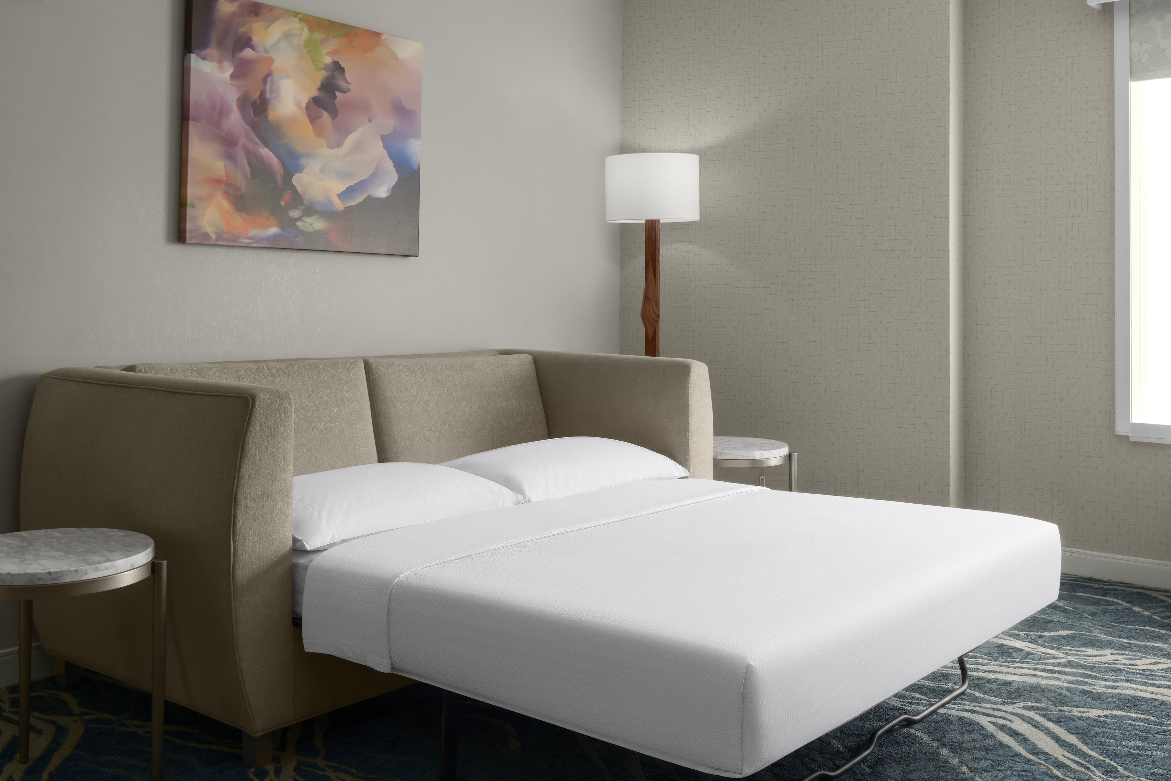 A hotel room with a bed, a nightstand, a lamp, and a painting on the wall.