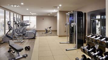 Une salle de sport équipée de tapis de course, de vélos elliptiques, d’un banc de musculation et d’un support à squats avec des haltères.
