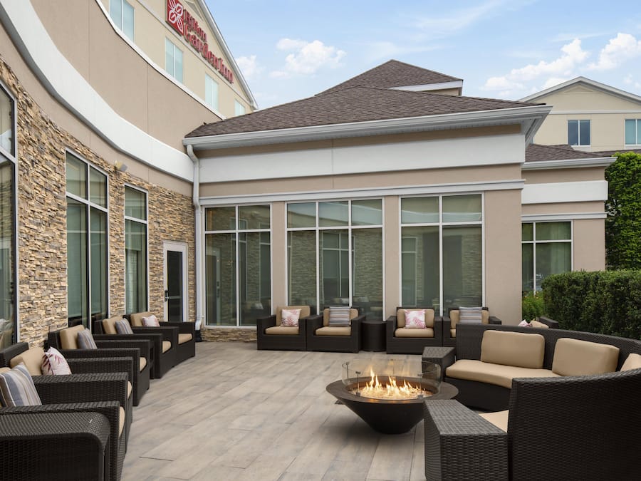 A hotel patio with wicker furniture, a fire pit, and large windows.