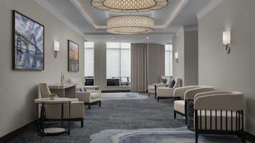 En hotellobby med en modern kristallkrona, en sittgrupp med fåtöljer och en soffa, en stor målning på väggen och utsikt över omgivningarna genom stora fönster.