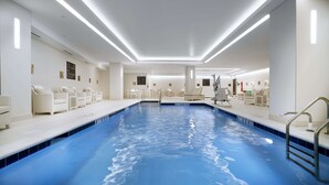 A modern indoor swimming pool with clear water, white walls, and lounge chairs along the sides. - Hilton Garden Inn Roslyn (Port Washington)