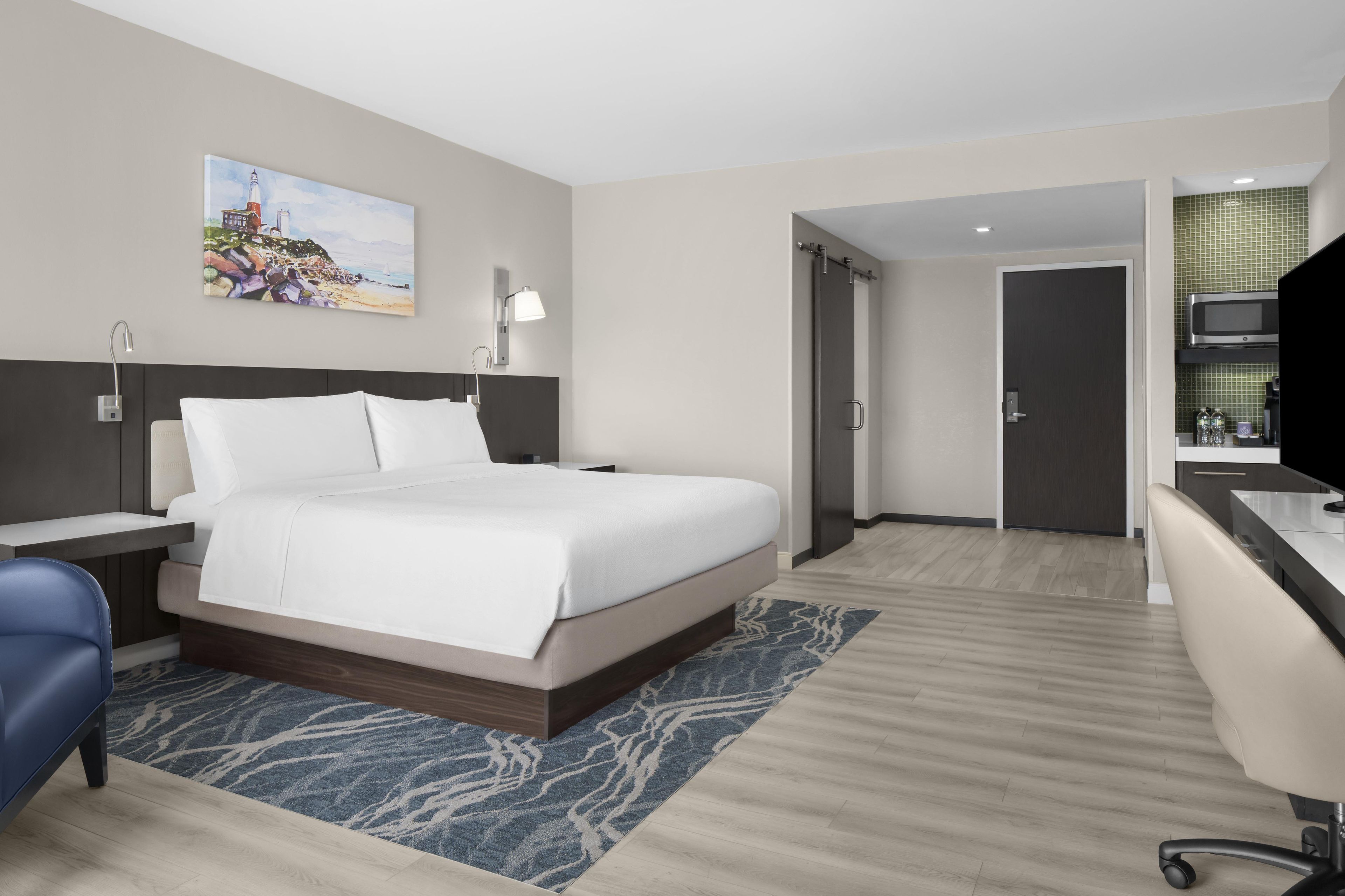 Une chambre d’hôtel moderne, équipée d’un lit, d’un bureau, d’une chaise, d’une télévision et d’un tableau au mur.