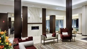 A modern lobby with a fireplace, seating areas, and a view of the city. - Hilton Garden Inn Roslyn (Port Washington)