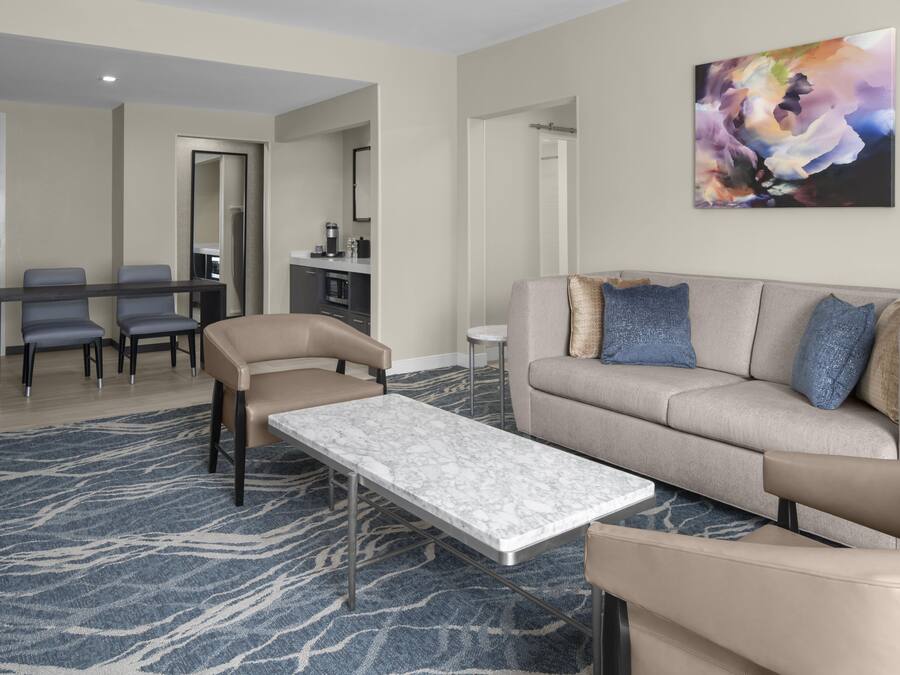 A modern living room with a sofa, armchairs, a coffee table, and a dining area with chairs and a table.