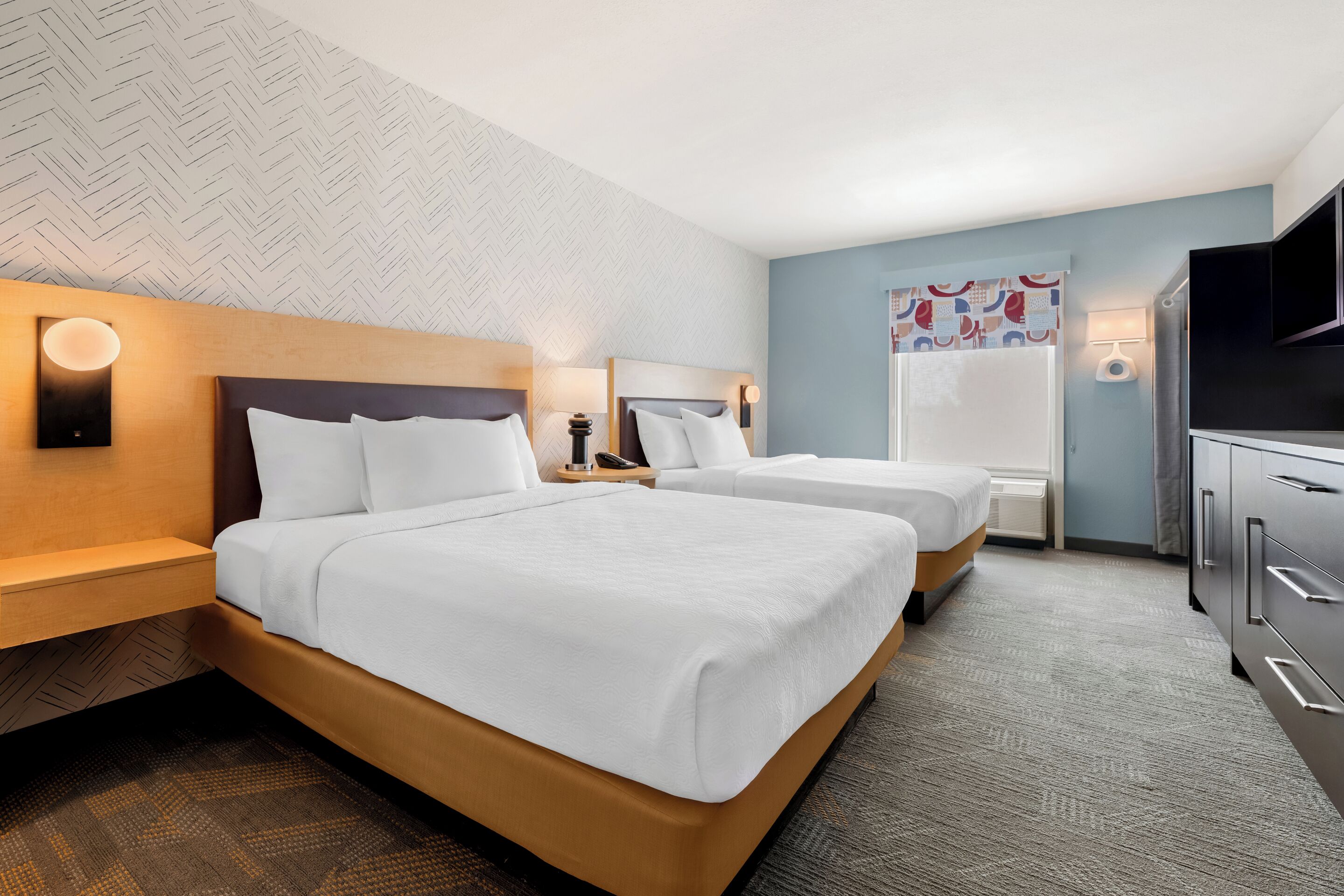 Hotelkamer met twee bedden, een houten hoofdbord, een nachtkastje, een lamp, een televisie en een muur met een visgraatmotief.