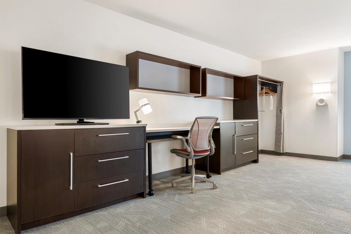A modern hotel room with a desk, chair, television, and wardrobe.