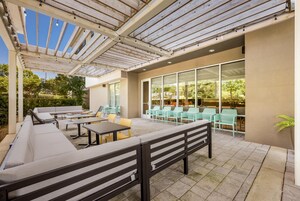 Un patio exterior con arreglos de asientos, incluyendo sofás y mesas, y una pérgola con luces colgantes.