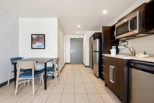 Una cocina moderna con electrodomésticos de acero inoxidable, una zona de comedor con mesa y sillas, y un pasillo que conduce a una puerta.