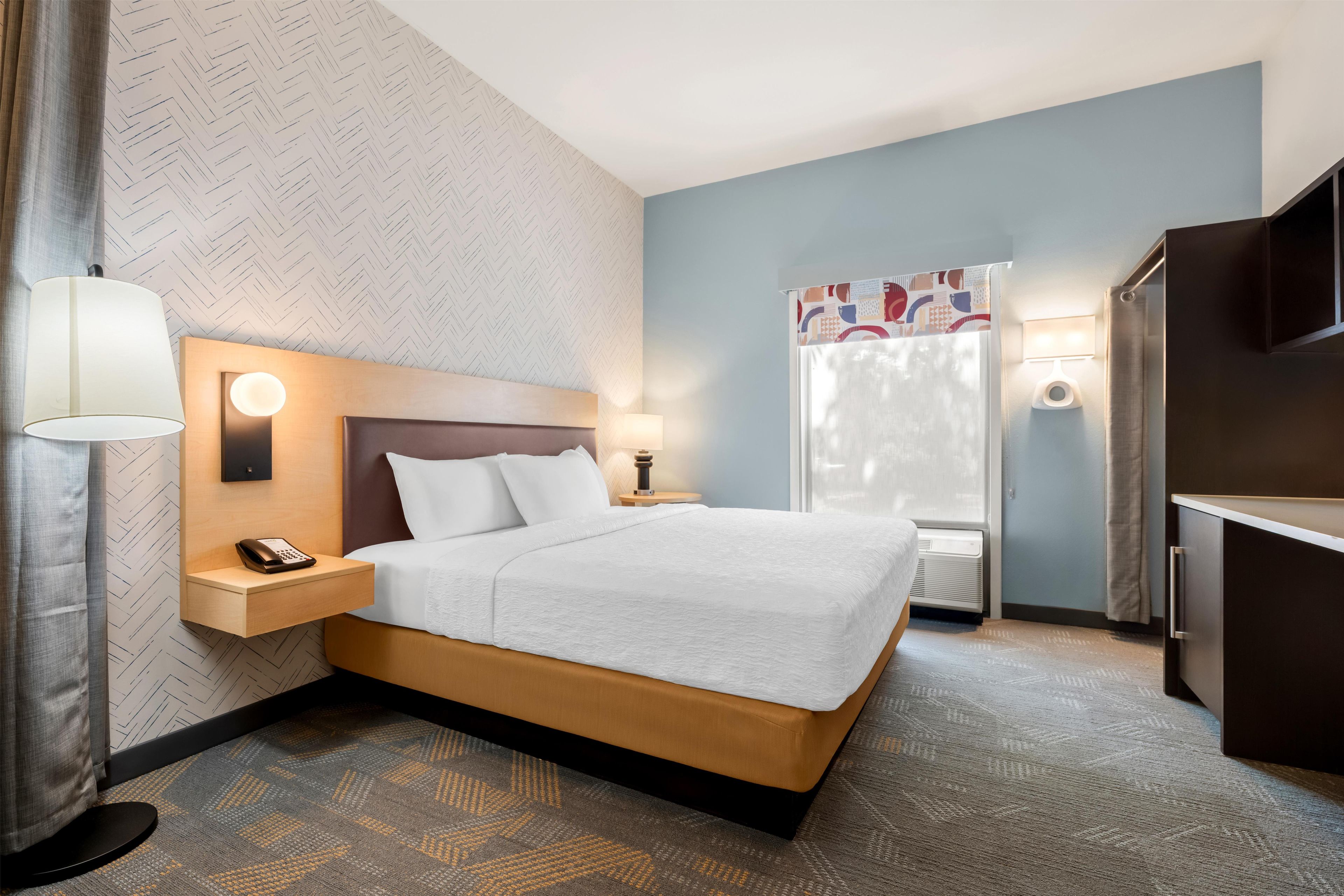 Une chambre d’hôtel équipée d’un lit, de lampes de chevet, d’un téléphone, d’une fenêtre avec des rideaux et d’un téléviseur.