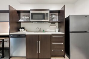 A compact kitchen with a built-in microwave, a dishwasher, and a refrigerator. - Home2 Suites by Hilton Prattville (Prattville)