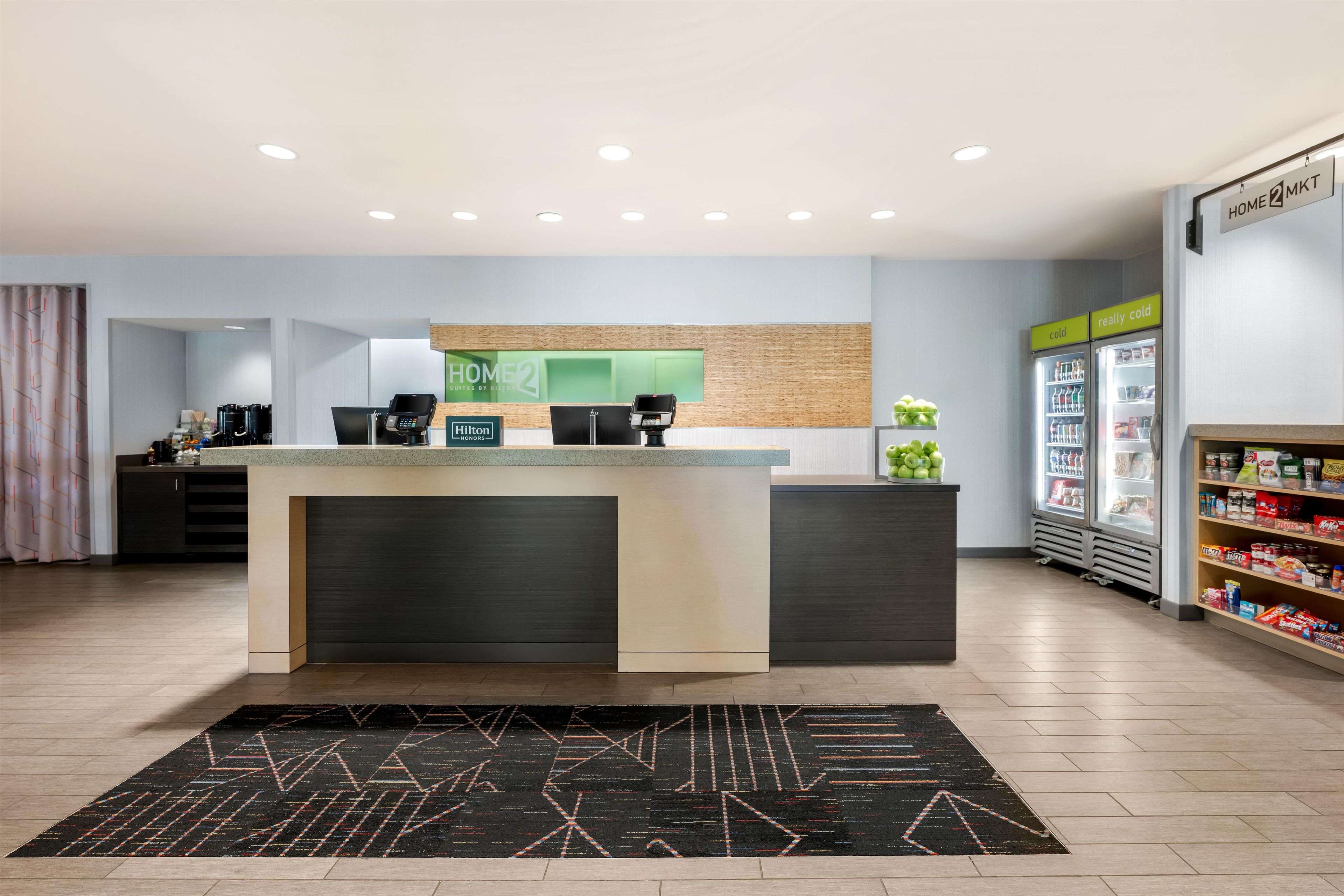 A hotel lobby with a reception desk, a minibar, a refrigerator, and a coffee station.
