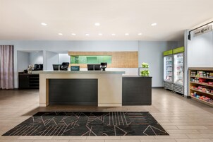 Un vestíbulo de hotel con mostrador de recepción, minibar, refrigerador y estación de café.