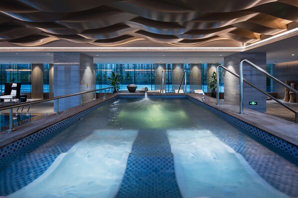 A modern indoor swimming pool with a view of the cityscape through large windows.