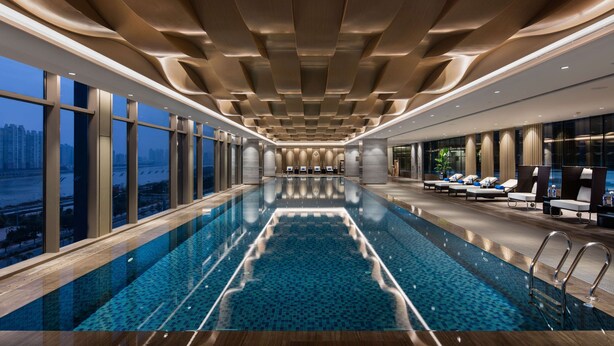 A modern indoor swimming pool with a view of the city skyline, sleek ceiling design, and comfortable lounging area. - Hilton Quanzhou Riverside (Quanzhou)