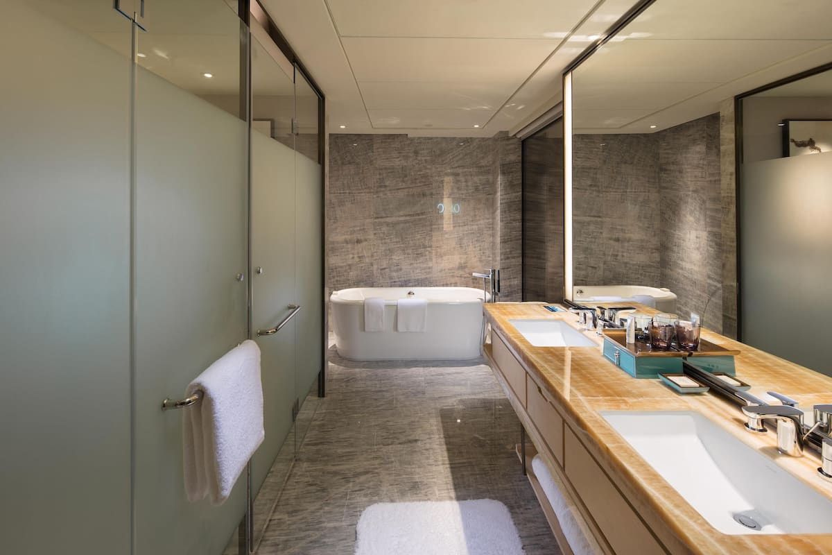A modern bathroom with a large bathtub, dual sinks, and a mirror.