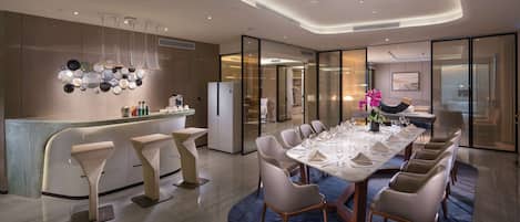 A modern dining area with a long table set for multiple guests, a bar with stools, and a contemporary light fixture above.