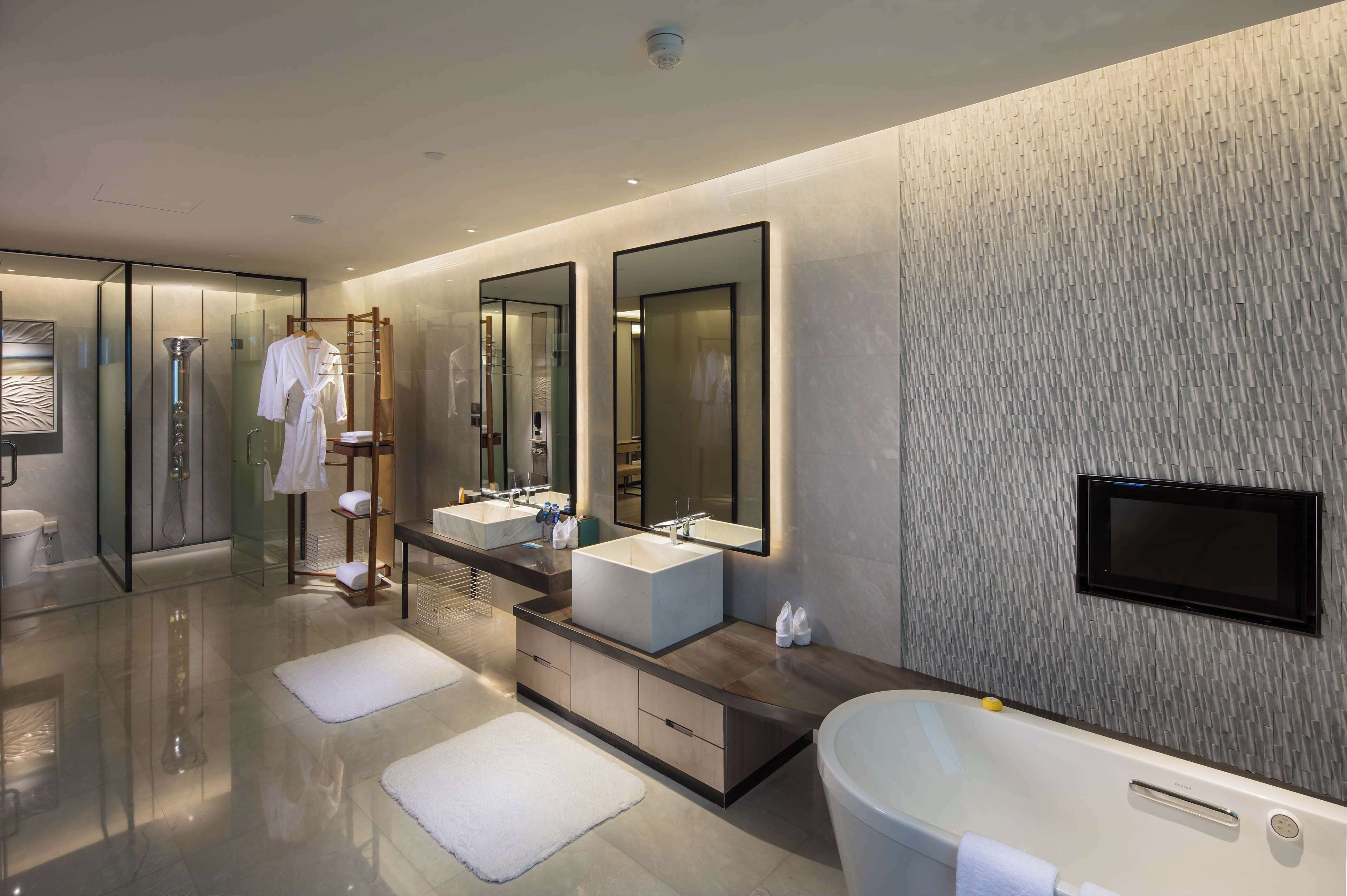 A modern bathroom with a large bathtub, two sinks, a walk-in shower, and a large mirror.