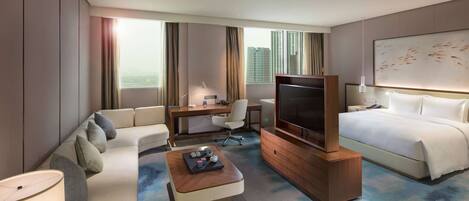 A modern hotel room with a sofa, a desk, a television, a bed, and a large window with curtains.