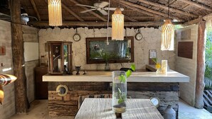 A rustic kitchen with wooden beams, a wooden table, hanging pendant lights, a clock, and a television. - Casa Tulum (Tulum)