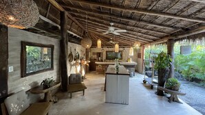 A rustic interior with a thatched roof, a bar area, seating, and a view of greenery outside. - Casa Tulum (Tulum)