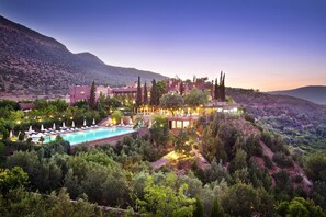 Relax by the resort's large pool surrounded by lush greenery and lounge areas with umbrellas, taking in the panoramic views of the surrounding landscape.