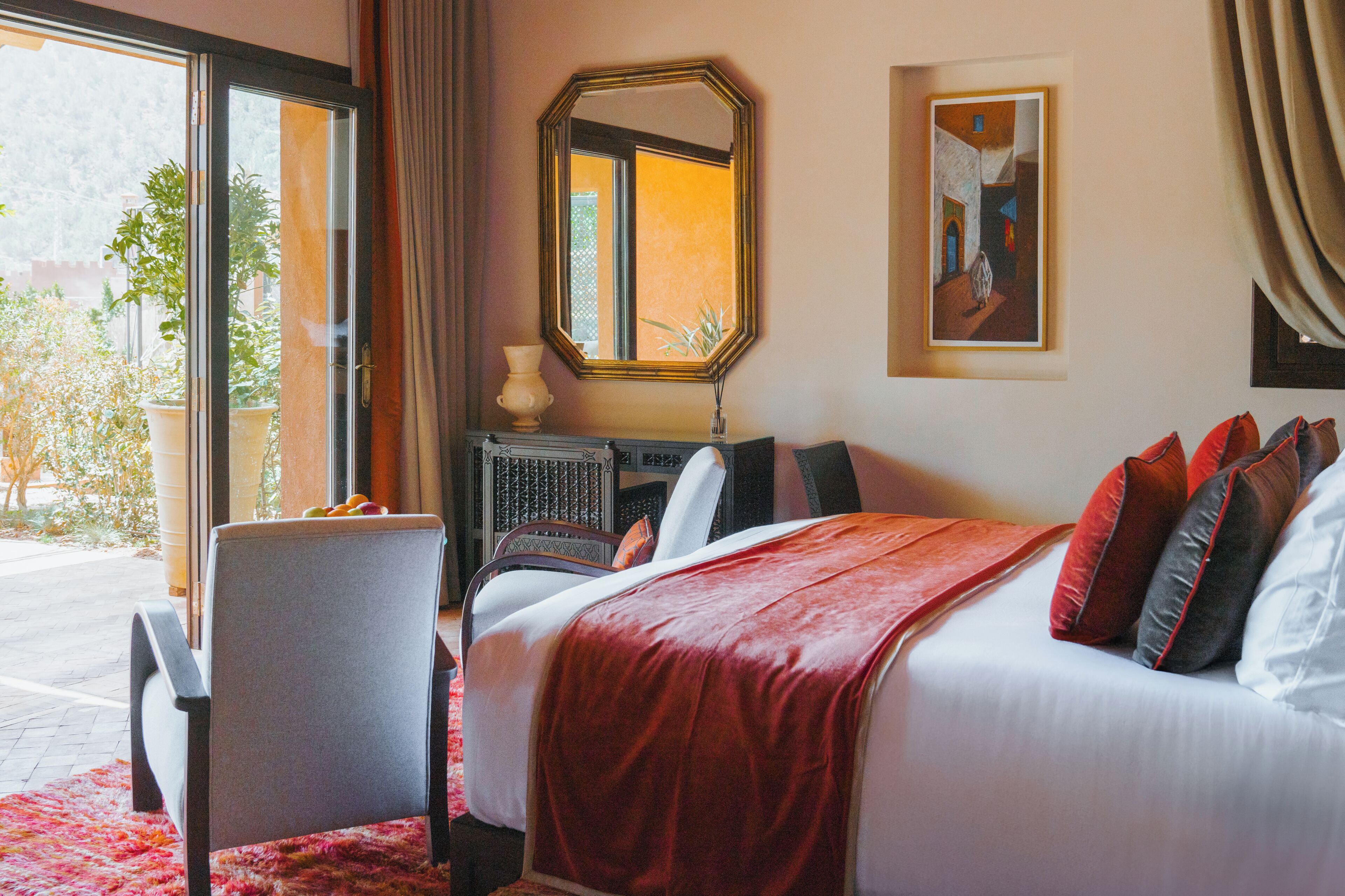 A hotel room with a bed, a chair, a desk, a mirror, and a painting on the wall.