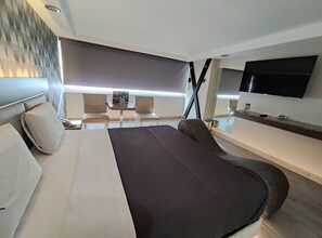 Une chambre d’hôtel moderne dotée d’un grand lit, d’une télévision à écran plat, d’une petite table avec des chaises et d’une fenêtre avec des stores.