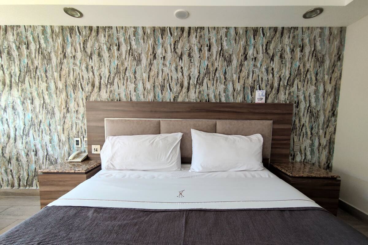 Ein Hotelzimmer mit einem großen Bett, zwei weißen Kissen, einem Holz-Kopfteil und einer strukturierten Wand.