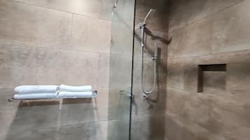 Un baño moderno con cabina de ducha de vidrio, un perchero con toallas dobladas y un pequeño hueco cuadrado en la pared.