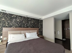 Een moderne hotelkamer met een groot bed, een hoofdbord met een marmerlook en een houten nachtkastje.