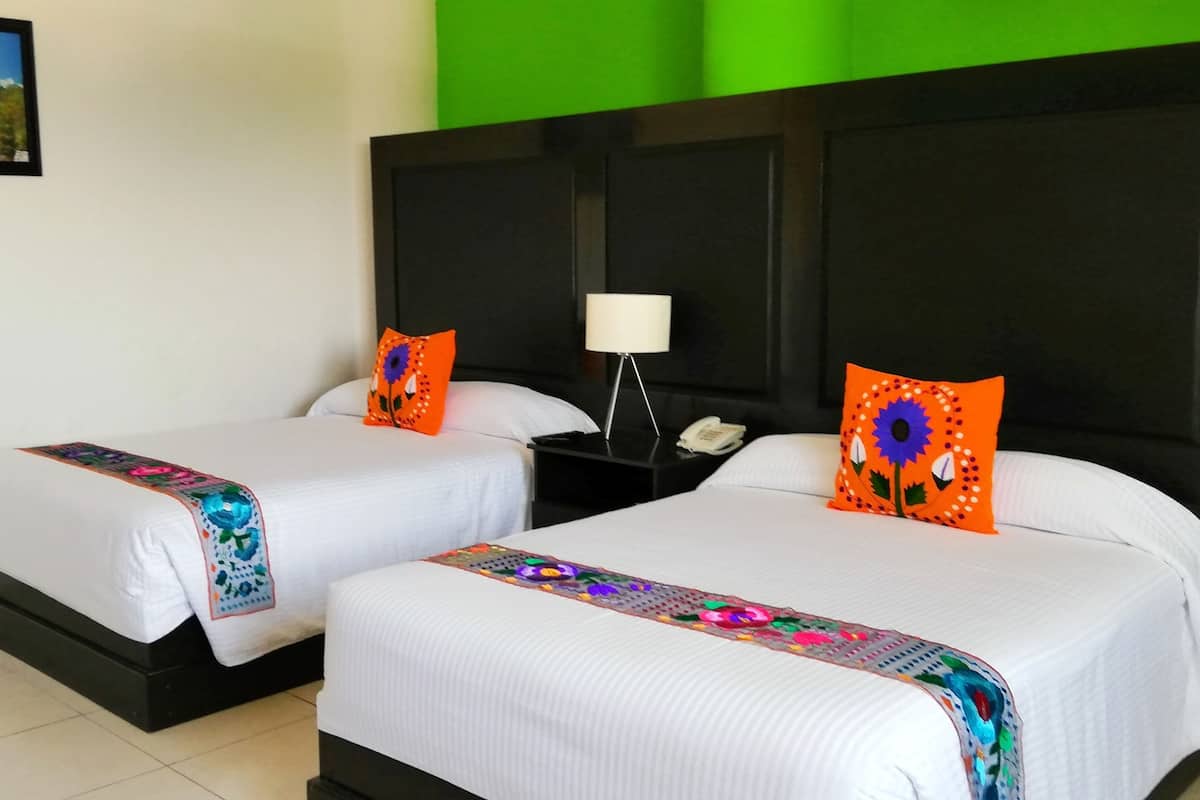 A hotel room with two beds, a nightstand with a lamp, and a green wall.