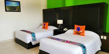A hotel room with two beds, a nightstand with a lamp, and a green wall.
