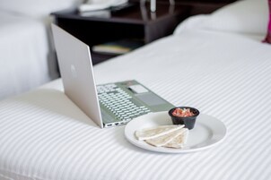 A laptop on a bed with a plate of food and a small bowl.