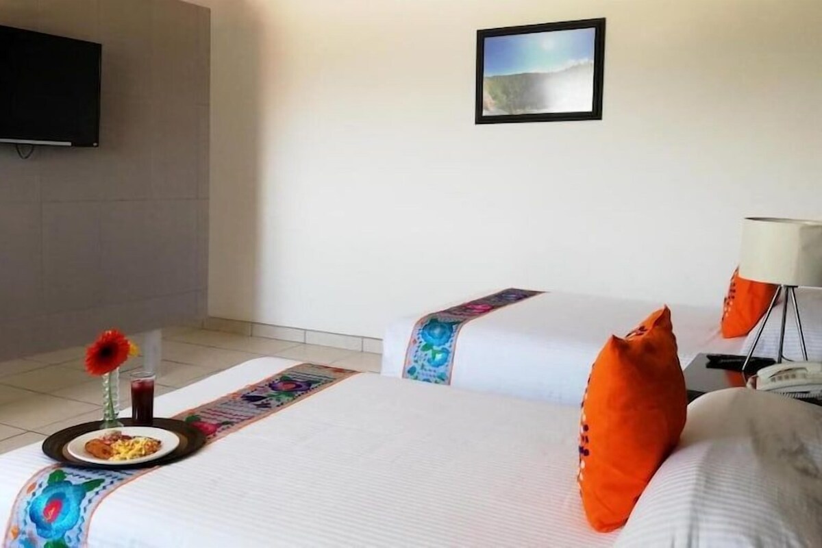 A hotel room with two beds, a flat-screen TV mounted on the wall, and a framed picture above the beds.