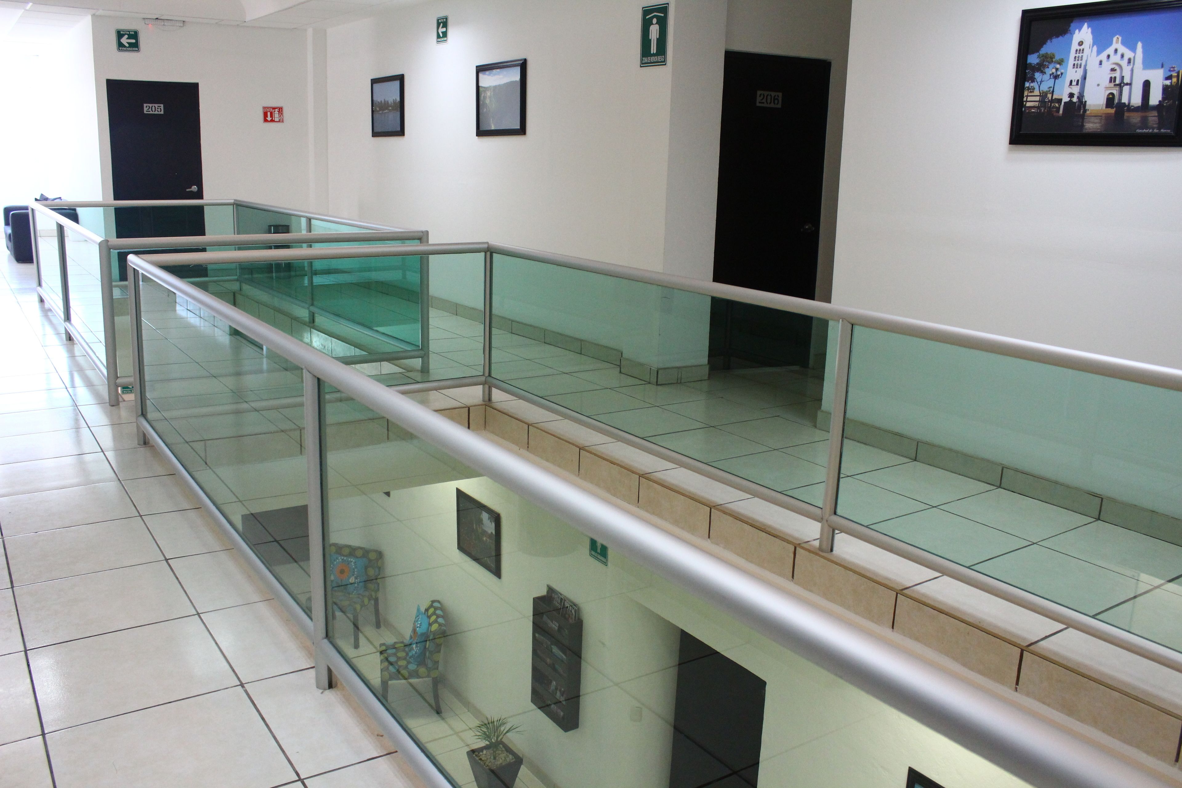 A modern indoor area with glass railings, tiled floors, and multiple doors labeled 205.