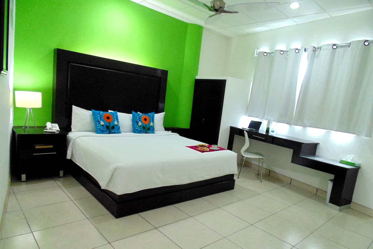 A bedroom with a bed, a desk, a chair, a nightstand, and a lamp.